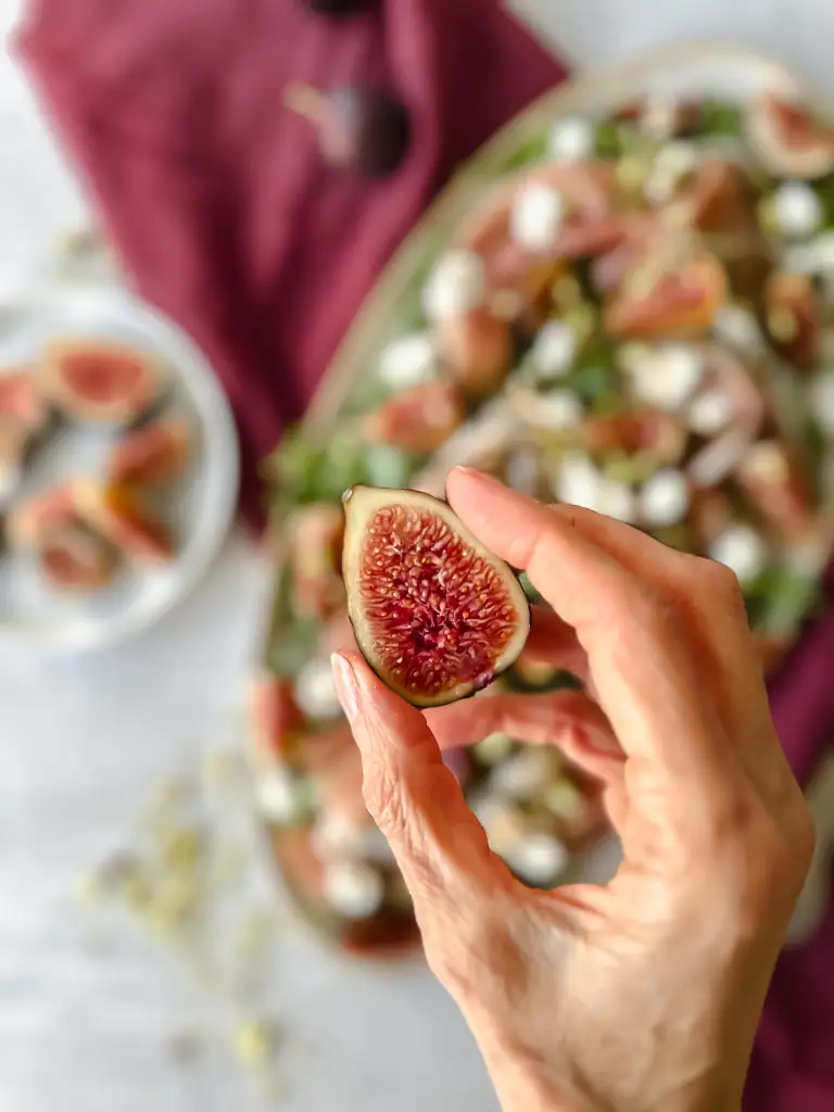 Fig in had halved, with fig and prosciutto salad in background