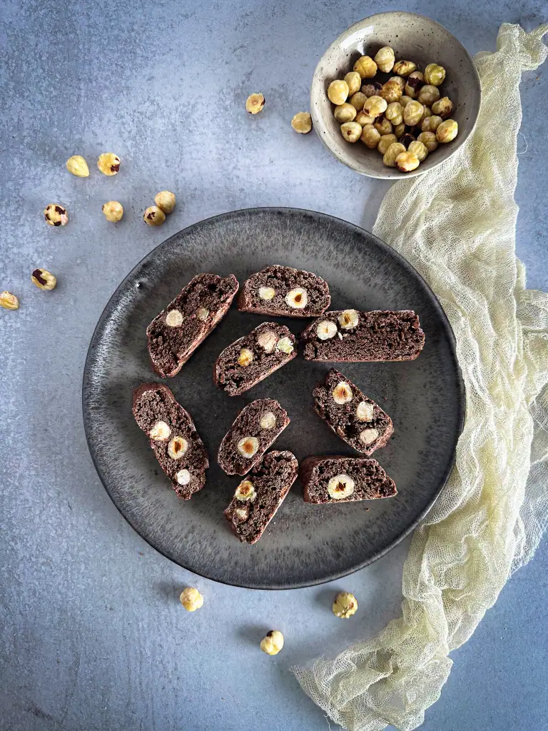 Italian Cocoa and Hazelnut Biscotti on a black plate with some hazelnuts in a bowl