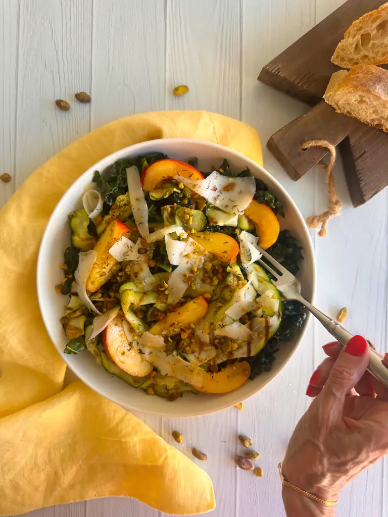 Hand with a fork eating the grilled zucchini, peach and kale salad