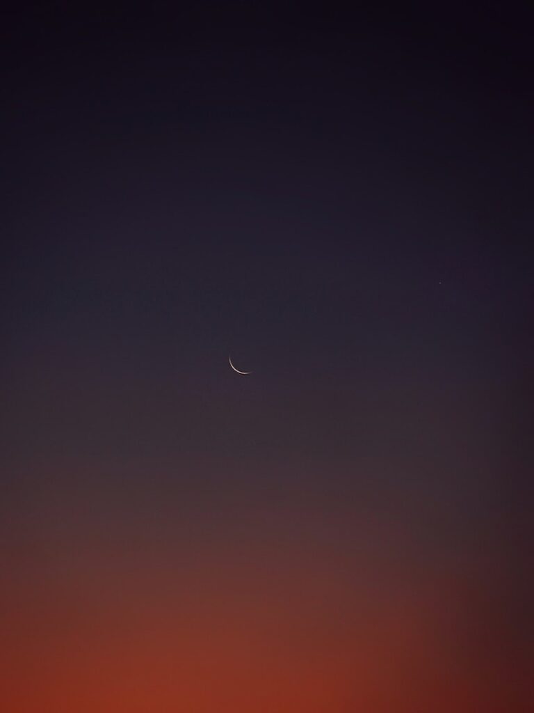 faint outline of moon against dark sunset background