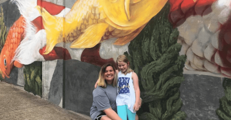 Katelyn Henderson smiles with her daughter in front of Huntsville mural