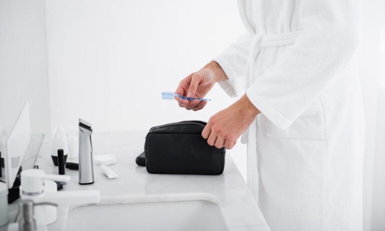 adult putting travel toothbrush in toiletry bag in hotel bathroom