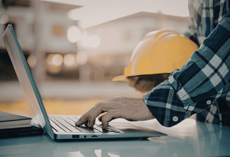 Person holding a hard hat and typing on a computer. You can only see the users hands.