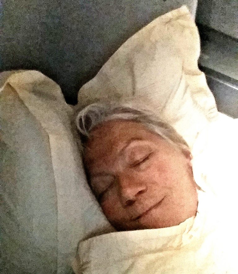 Stacey laying flat with head on Business Class pillow - blanket pulled to chin