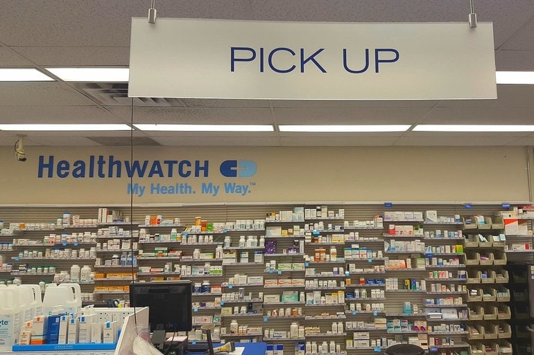 A pharmacy counter with medication on the shelf and pick up board on the top