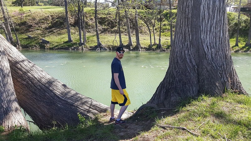 Buddy standing between two large trees as he looks into the river for fish and turtles