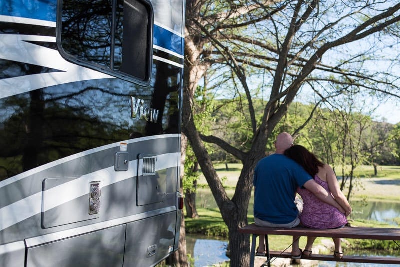 Brooke and Buddy sitting on a picnic table next to their RV embracing slow travel