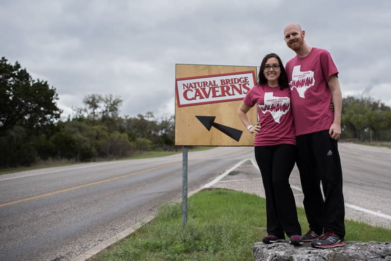 Brooke and buddy in their t-shirts posing by the natural bridge caverns in Texas sign