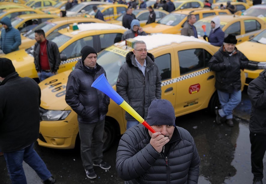 FILE - In this Wednesday, Feb. 13, 2019, file photo a taxi driver blows into a horn during a protest against ride hailing services in Bucharest, Romania. The Romanian government has issued an emergency decree ramping up steep fines for drivers of ride-hailing services like Uber and Taxify. The decree taking effect Thursday, May 16, 2019 fines drivers transporting people in their car without a valid taxi license up to $1,175 (1,050 euros) already from the first offense. Previously, drivers were fined only after repeated offenses. (AP Photo/Vadim Ghirda, File)