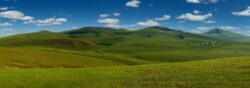 Mongolija putovanje: panorama talasaste zelene mongolske stepe sa jurtama u daljini