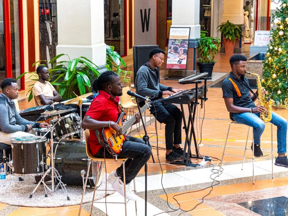Band performing with drums, guitars, keyboards, and saxophone in a shopping mall