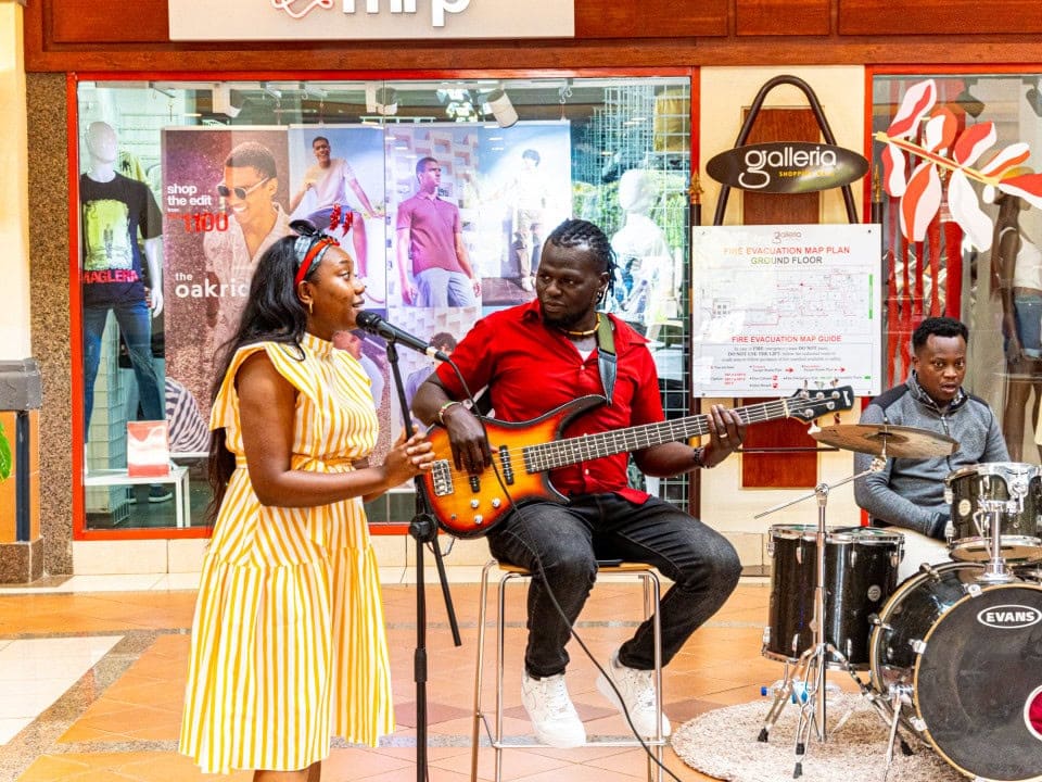 Woman singing beside a seated bass guitarist and drummer