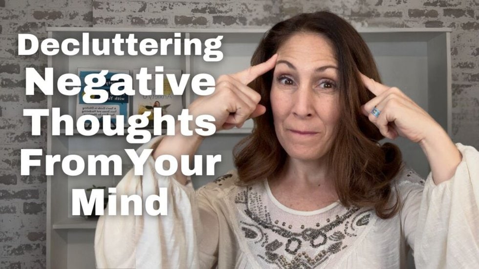 Dr. Jodi Aman pointing to her temples with a thoughtful expression, wearing a white embroidered blouse. The text on the image reads, "Decluttering Negative Thoughts in Your Mind."