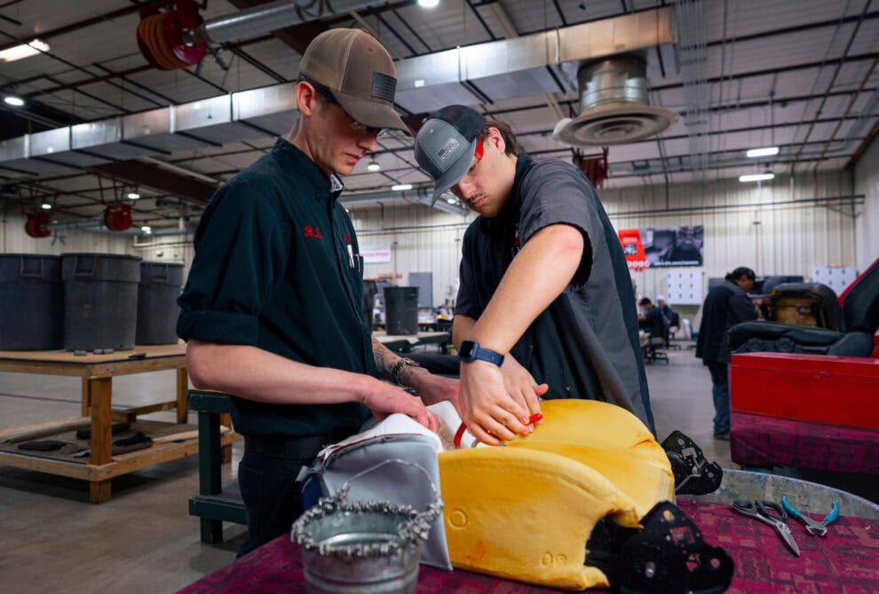 Two students adding upholstery to bucket seat.