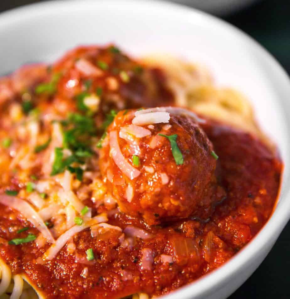 Baked meatballs over pasta with Parmesan cheese and herbs on top