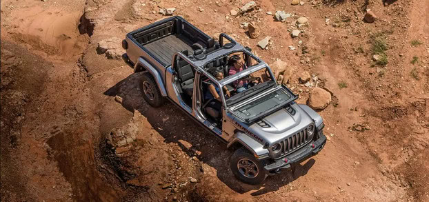 Aerial view of a silver Jeep Gladiator driving on rocky terrain.