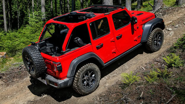 Red Jeep Wrangler driving along a small off-road path surrounded by woods.