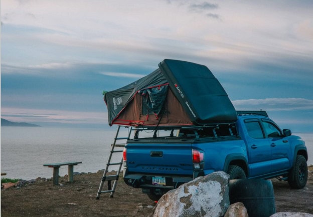 Blue Toyota Tacoma with iKamper Rooftop Tent overlooking ocean