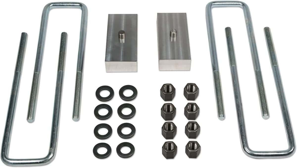 Four U-bolts, two spacers, and some nuts and bolts lie on a white background spaced evenly.