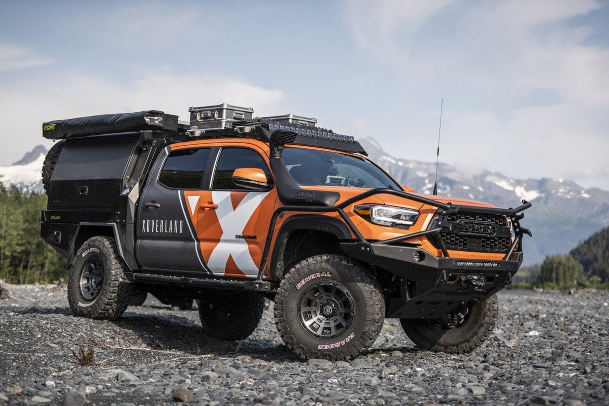 An orange and black overland Toyota Tacoma parked on a gravel road