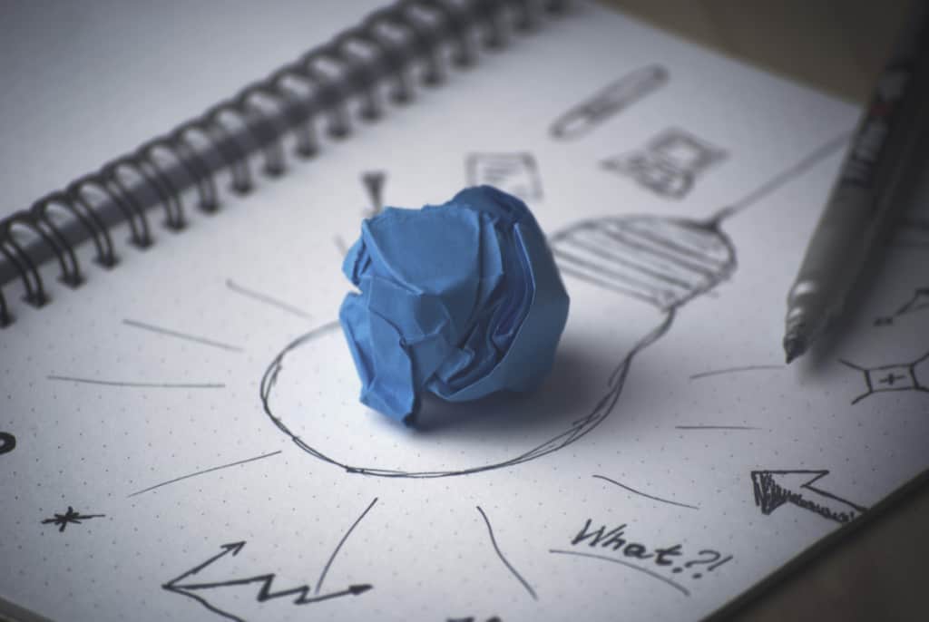 Blue crumpled paper in the middle of lightbulb drawn on a sketchpad