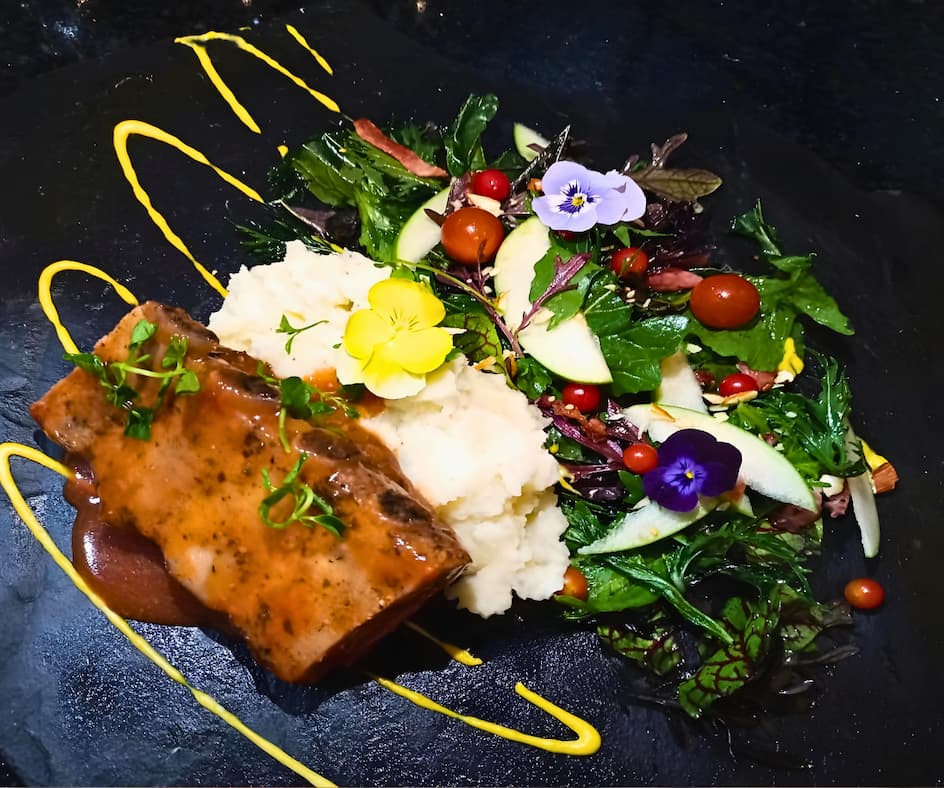 Deliciosa posta cartagenera servida sobre puré de yuca con ensalada elegante