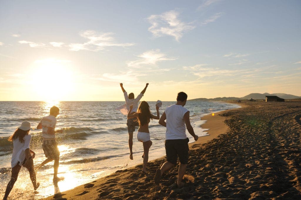Group of friends running and jumping on the beach at sunset
