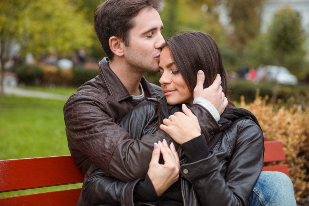 Romantic young couple hugging on a park bench during autumn, sharing an intimate first date moment.