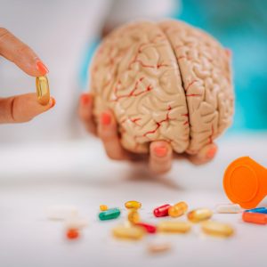 Cognitive improvement or brain supplements. Woman holding a supplement capsule and a model brain.