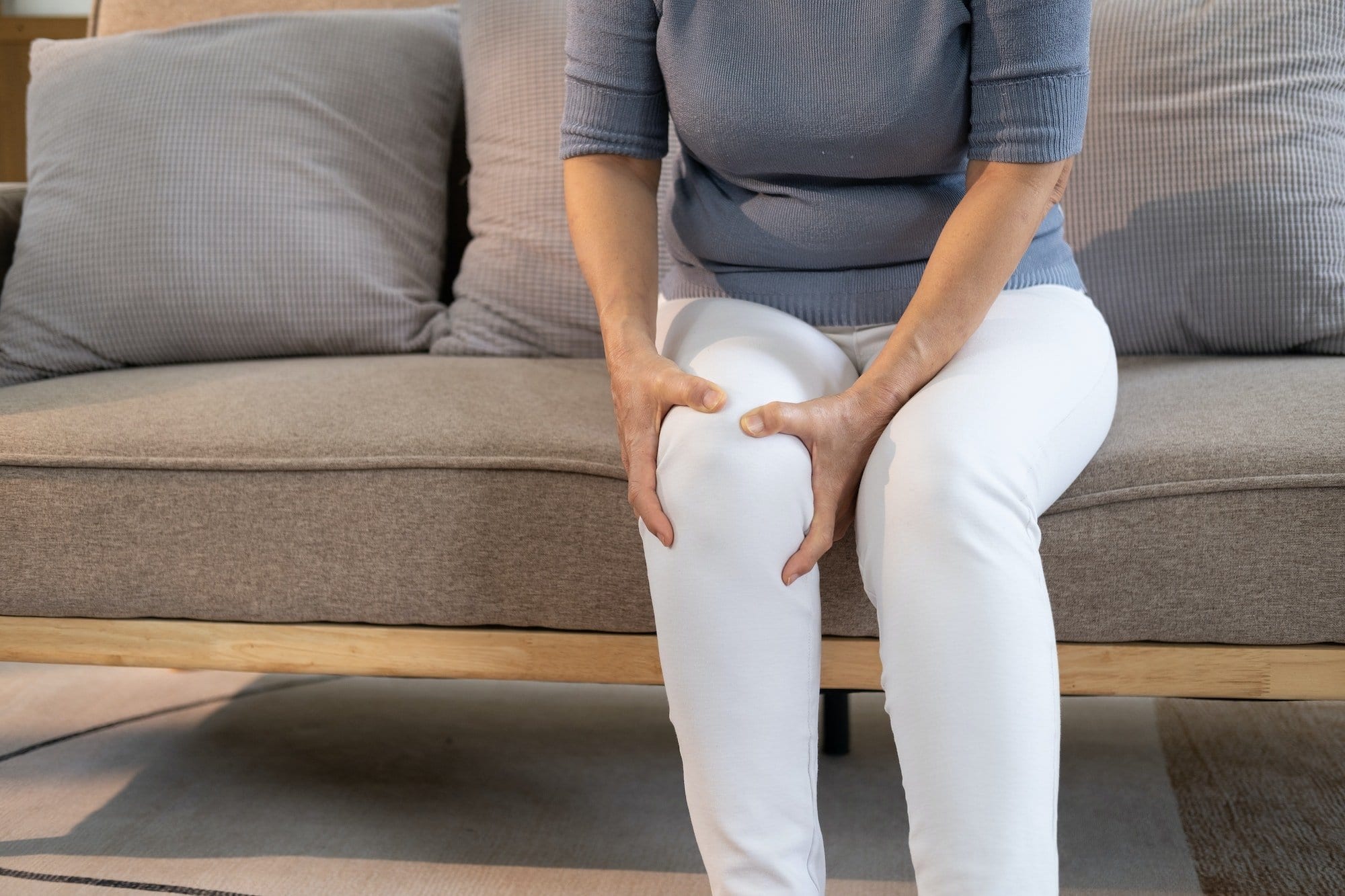 Elderly woman massaging the knee easing the aches. Joint pain concept.