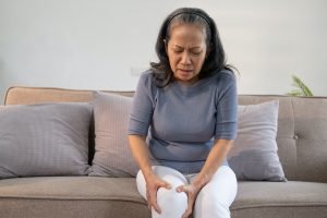 Elderly woman massaging the knee easing the aches. Joint pain concept.