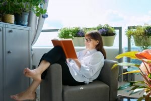 Middle-aged relaxed happy woman reading book, sitting at home