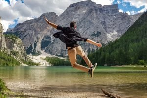Rear view of man jumping on wooden deck by lake. Happy person in idyllic place in nature.
