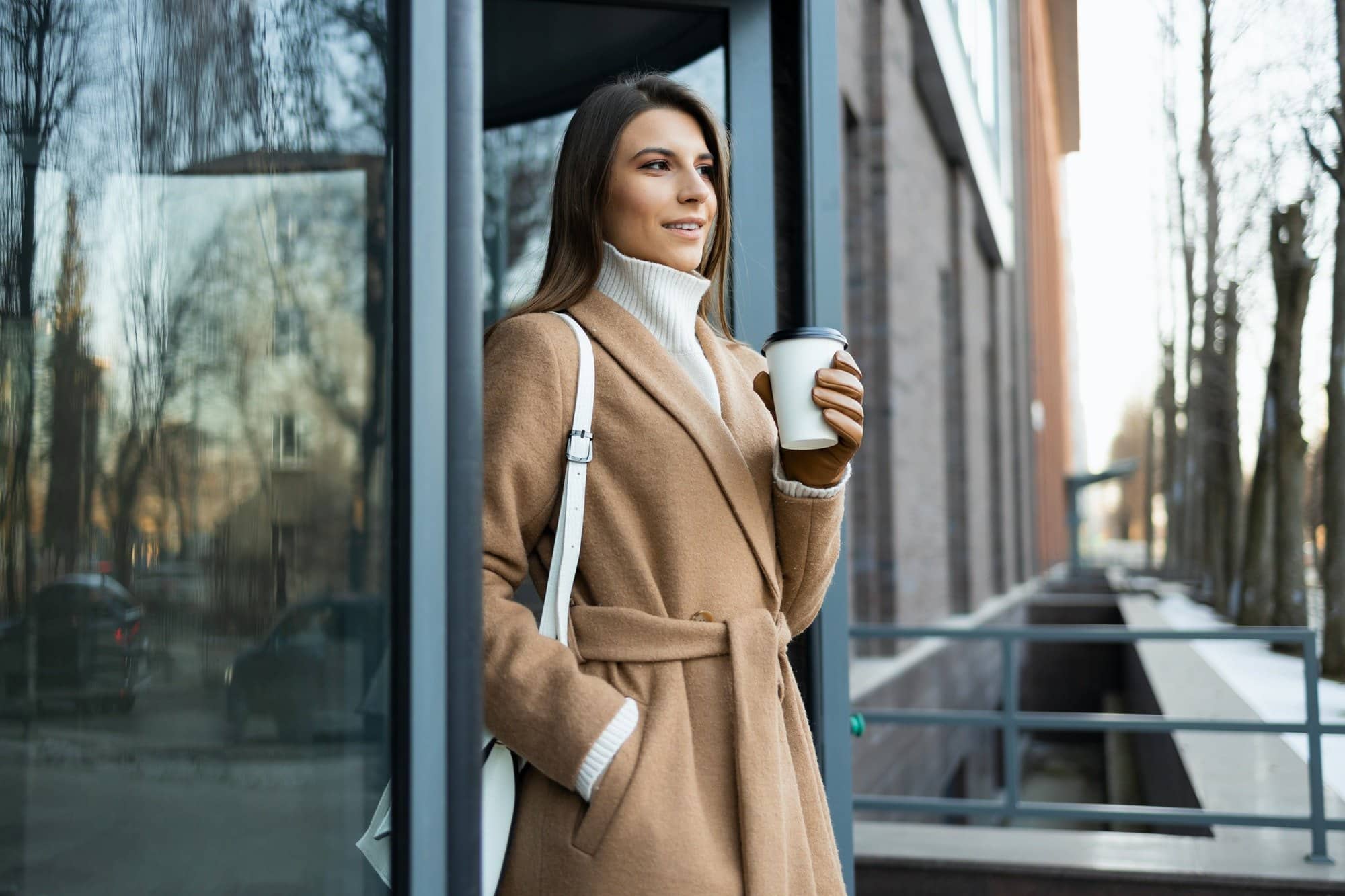 Young brunette in a brown coat with a cup of coffee in her hand