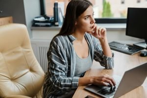 Charming thinking woman working with laptop while sitting at table