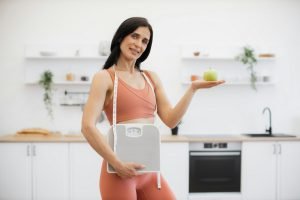 Health coach with measuring tape, scales and apple at home