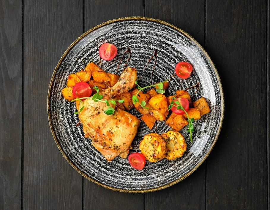 Roasted chicken thigh with fried pumpkin, grilled corn on the cob and tomato