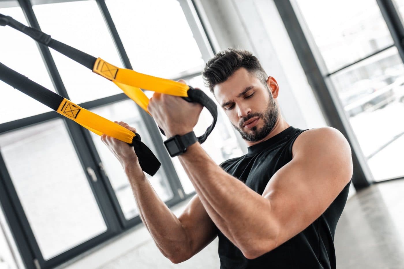 handsome muscular young man looking at biceps while training with suspension straps in gym