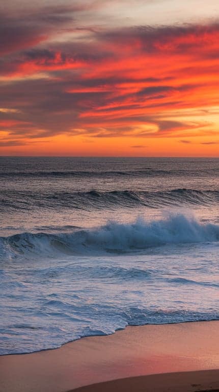 A vibrant sunset over the ocean with waves and colorful clouds.