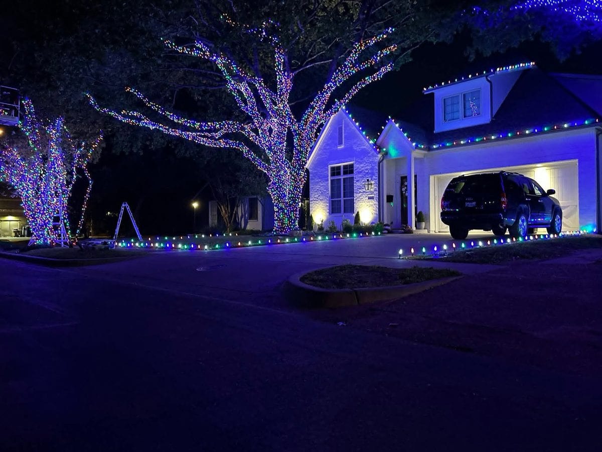 Upscale home with blue and purple lit trees and multicolor ground lights