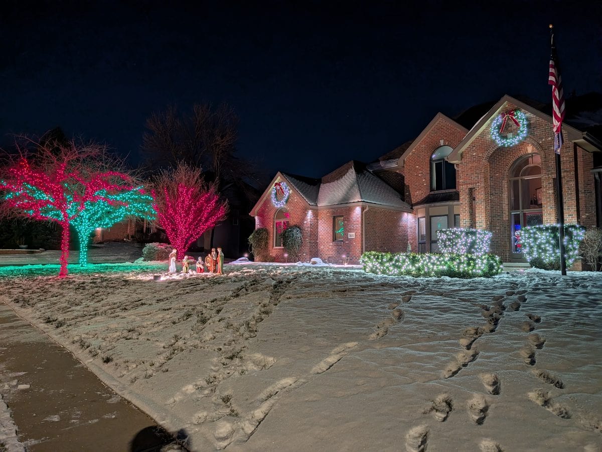 Brick home with colorful lit trees and bushes in fresh snow