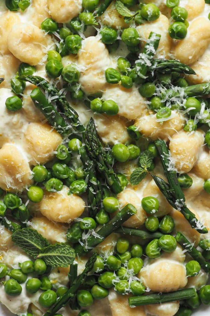 Spring on a plate with these 10-Minute Creamy Gnocchi with Peas and Asparagus. It's really that quick and so delicious! To speed things up I use pre-made gnocchi; then, there are bright peas and asparagus to make the most of seasonal ingredients. These are mixed with a creamy lemony garlicky white sauce that is to die for. And finally, some grated parmesan and mint leaves to top it all. | Paula's Apron Recipe