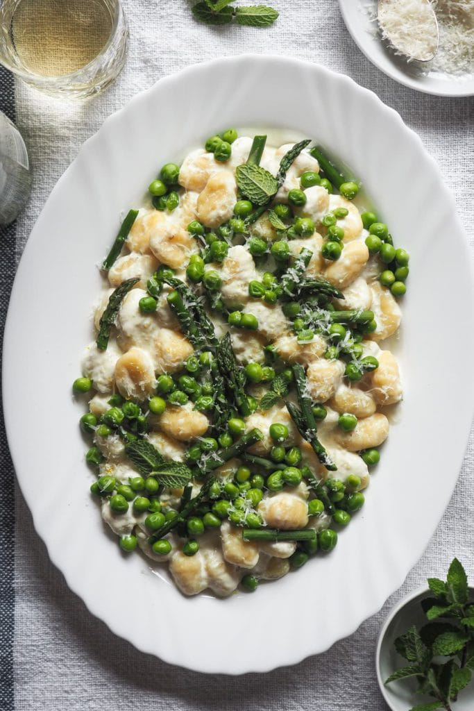 Spring on a plate with these 10-Minute Creamy Gnocchi with Peas and Asparagus. It's really that quick and so delicious! To speed things up I use pre-made gnocchi; then, there are bright peas and asparagus to make the most of seasonal ingredients. These are mixed with a creamy lemony garlicky white sauce that is to die for. And finally, some grated parmesan and mint leaves to top it all. | Paula's Apron Recipe