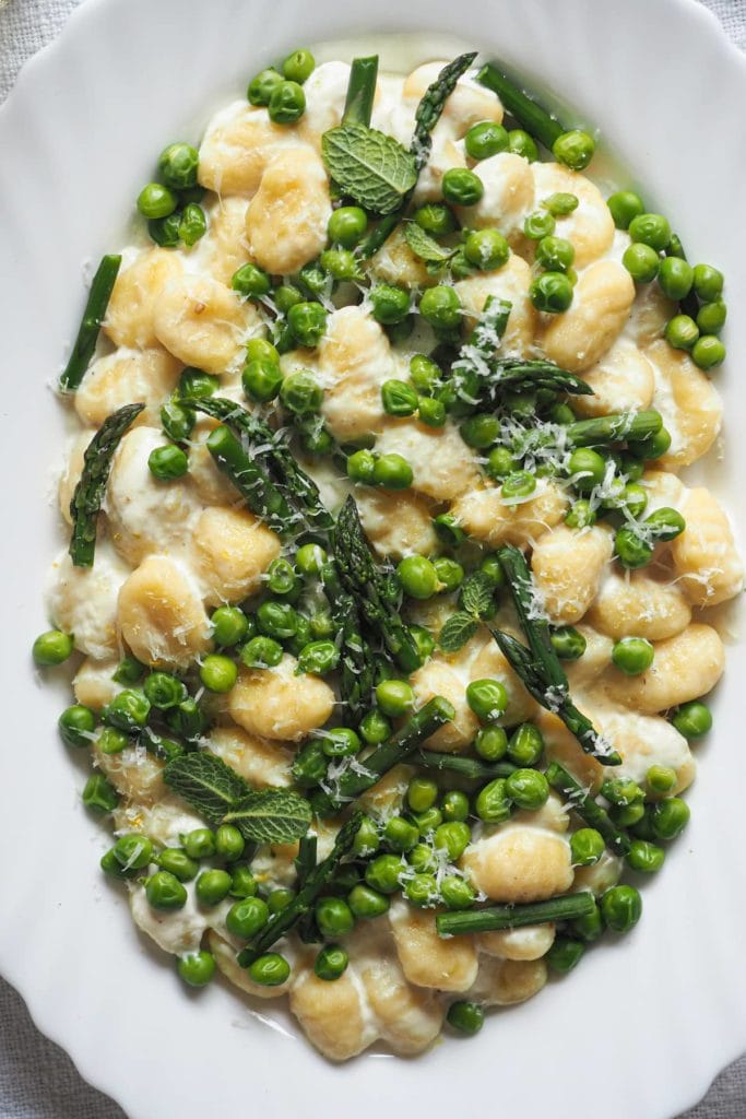 Spring on a plate with these 10-Minute Creamy Gnocchi with Peas and Asparagus. It's really that quick and so delicious! To speed things up I use pre-made gnocchi; then, there are bright peas and asparagus to make the most of seasonal ingredients. These are mixed with a creamy lemony garlicky white sauce that is to die for. And finally, some grated parmesan and mint leaves to top it all. | Paula's Apron Recipe