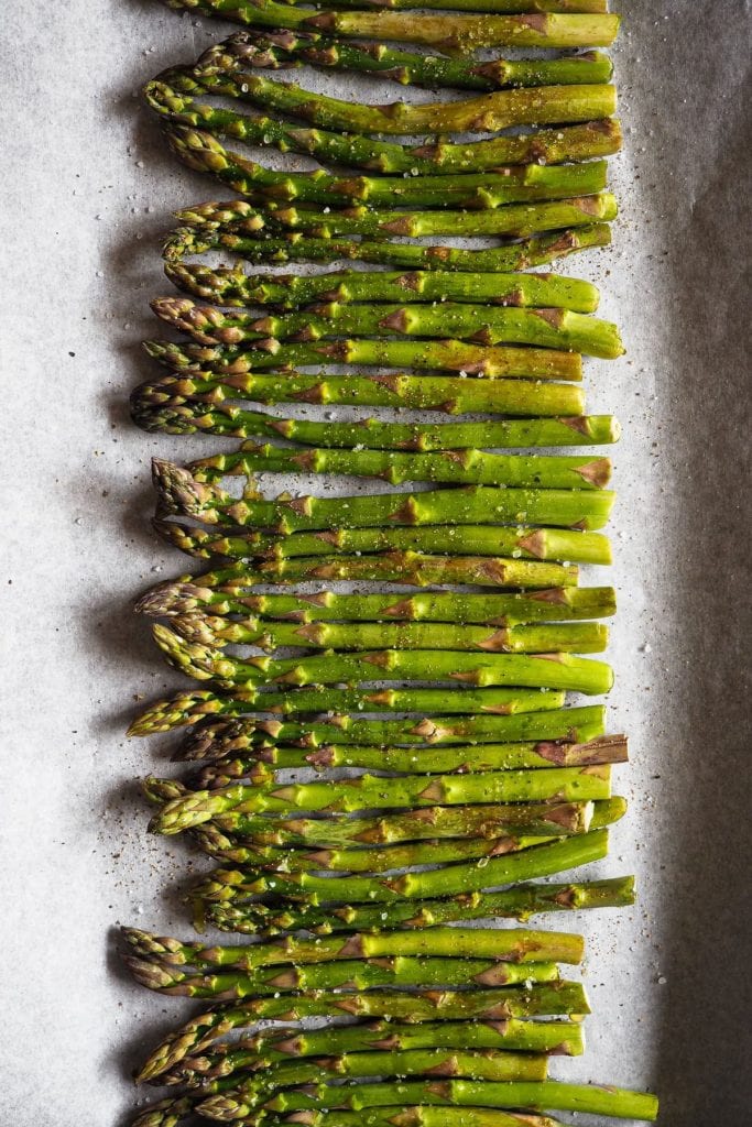 These Garlicky Lemony Crispy Roasted Asparagus are an ideal side dish during spring. Imagine grilled asparagus (because a high-temperature oven cooks them in a similar way :P), but with extra crunchiness and flavour thanks to a garlic, lemon and hazelnut topping! It's perfect to change from classic roasted asparagus, and even those who say they're not the biggest fans of asparagus can't resist these. On this shot we can see the asparagus with olive oil and seasoned on a tray before getting into the oven. | Paula's Apron Recipe