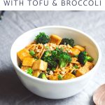 Spicy noodles with tofu and broccoli in a serving bowl next to a wood spoon.