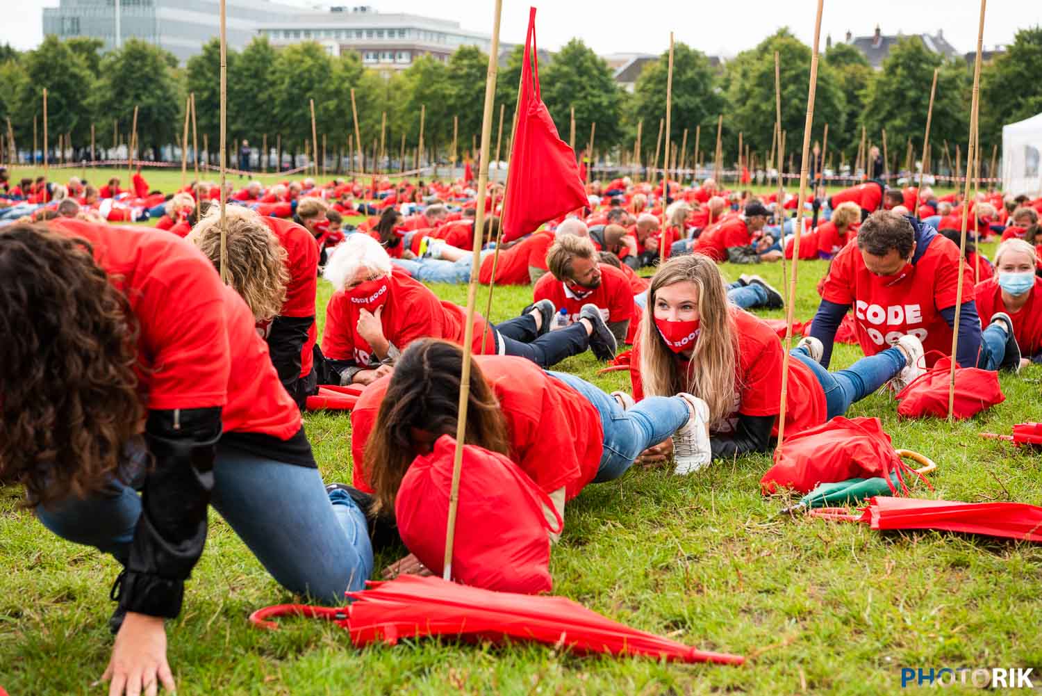 People participating in a large outdoor protest or demonstration in a park, dressed in red with protest signs and flags, engaging in a coordinated activity, indicative of social activism or rally.