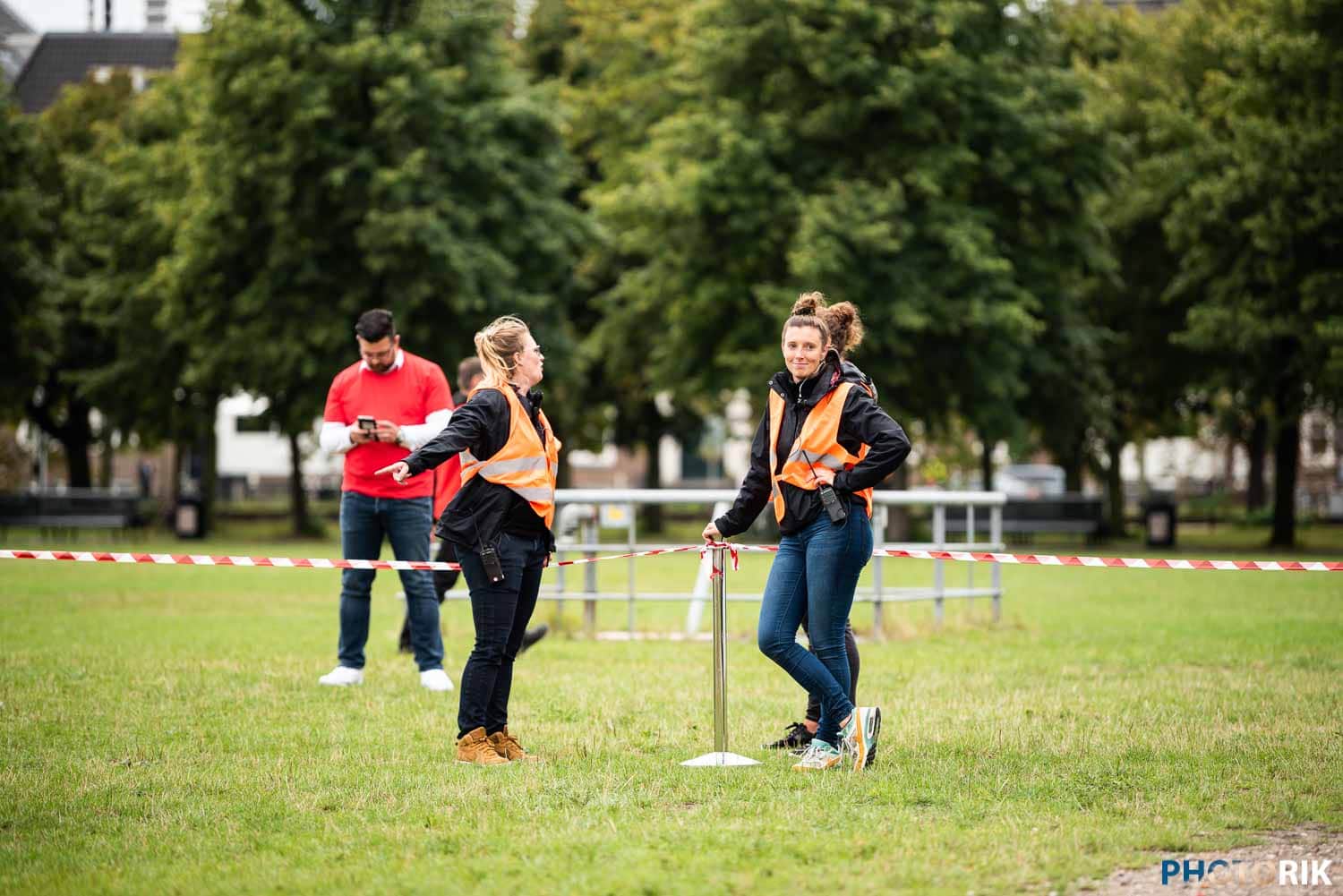Emergency response team members coordinating at an outdoor scene, wearing high-visibility vests, discussing incident management, in a park environment, during daytime.