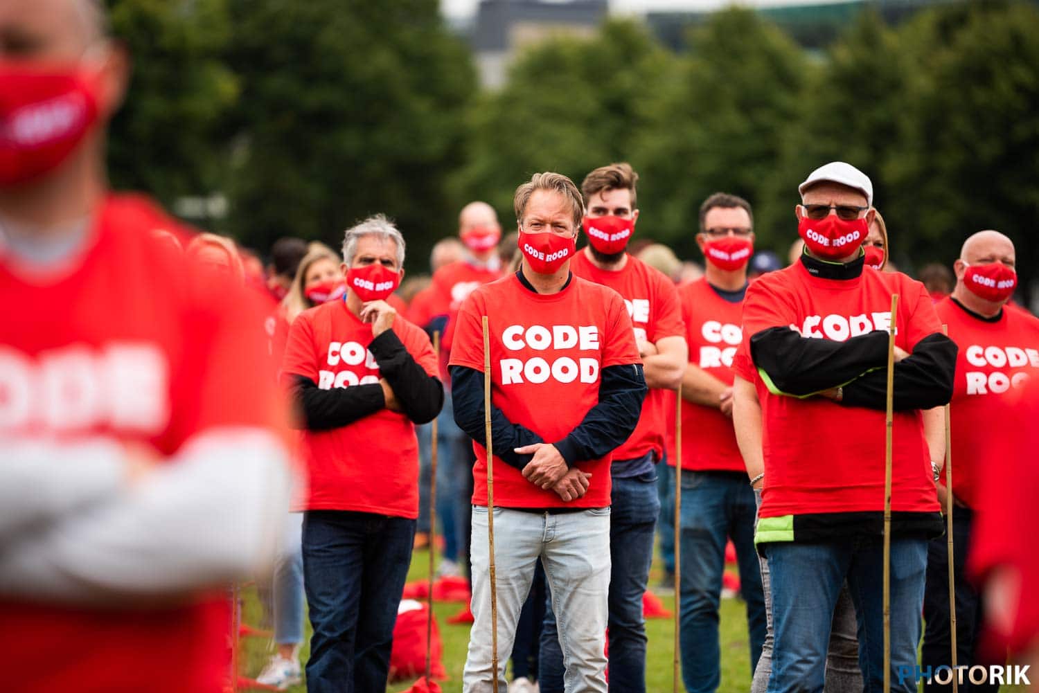Participants wearing red "CODE ROOD" face masks and T-shirts at outdoor event, raising awareness for climate change action, outdoor rally, environmental protest, activism, community gathering.