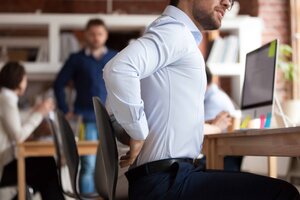 Businessman Sitting In Shared Office Suffers From Lower Back Pain 